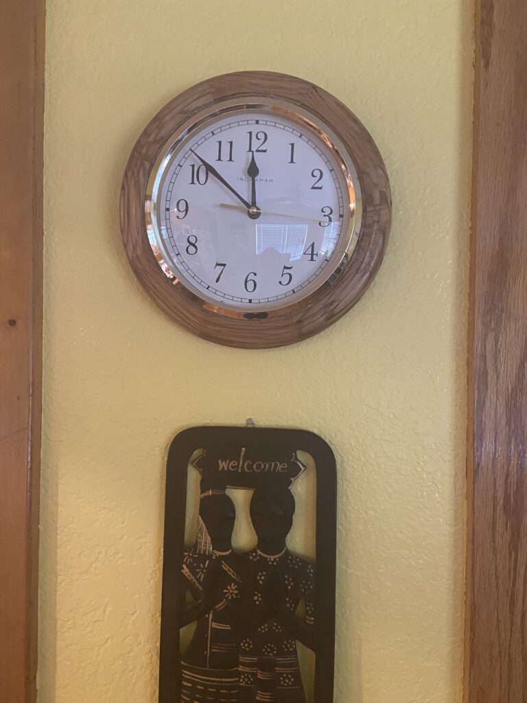 simple, round clock hangs on a yellow wall, African art displaying Welcome hangs just below it