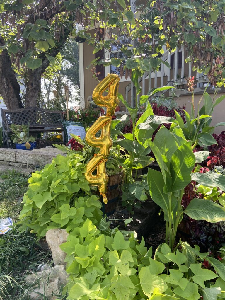 Beautiful landscaping with ivy, cannas, red coleus, an iron and wood bench, RR ties, and rock are the background for 3 number 4s stacked on top of each other, set in the middle of the photo. They appear to lean a little to the right, just slightly.
