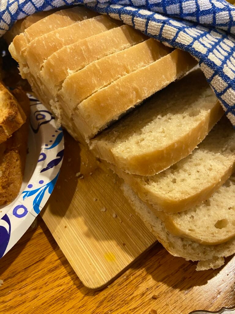 sliced homemade bread lays on a wooden cutting board with a blue and white checkered towel covering it